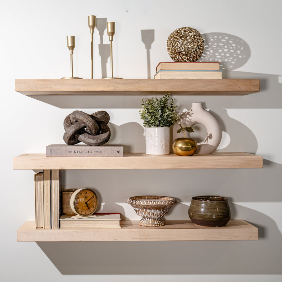 Three solid maple floating shelves styled with candlesticks, books, plants and pottery