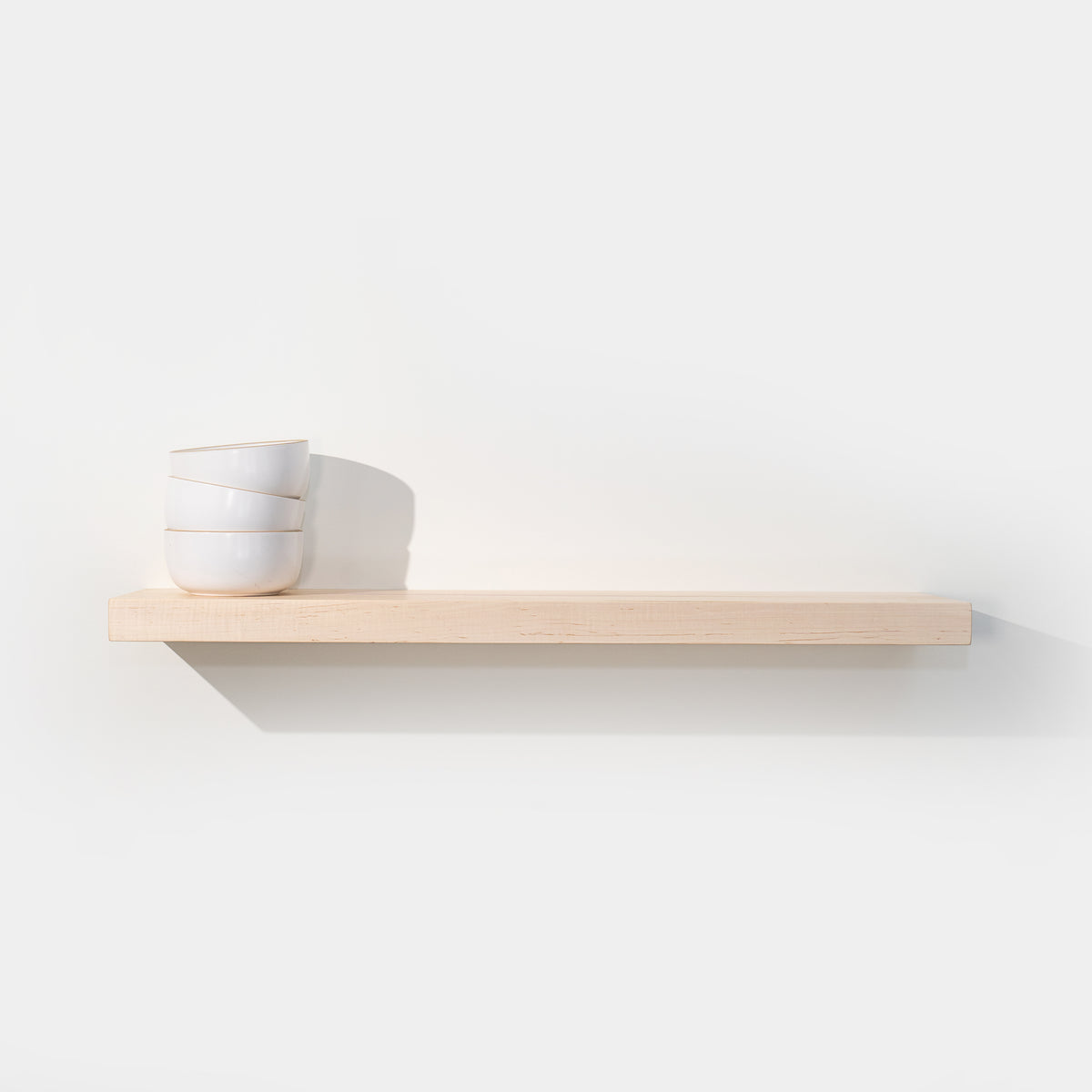 Solid maple floating shelf with stacked white bowls on a white wall
