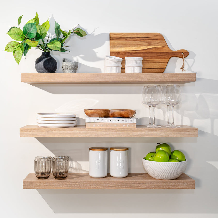 Three solid white oak floating shelves styled with plants, dishes, glassware and a cutting board